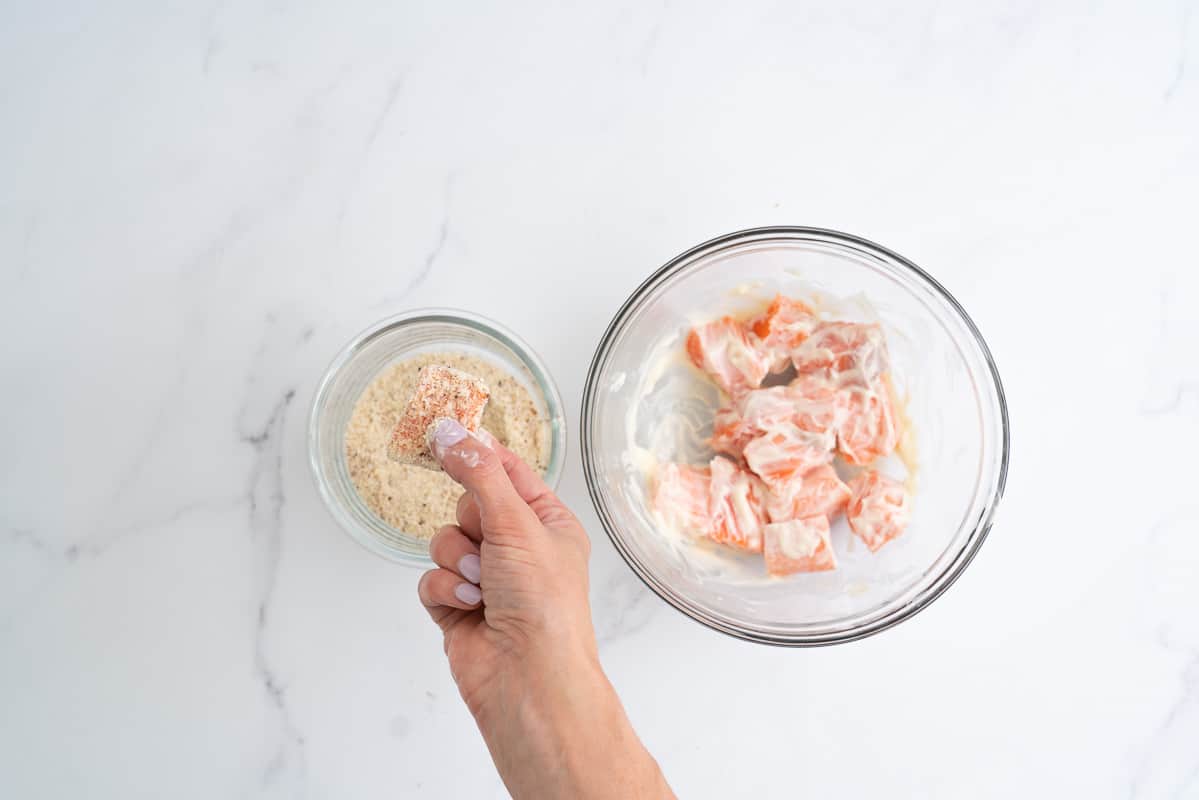 A bowl of salmon coated in mayonnaise, alongside a bowl of ground almonds.