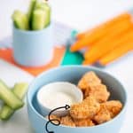 A blue bowl filled with salmon nuggets, cucumber and carrot sticks in the background.