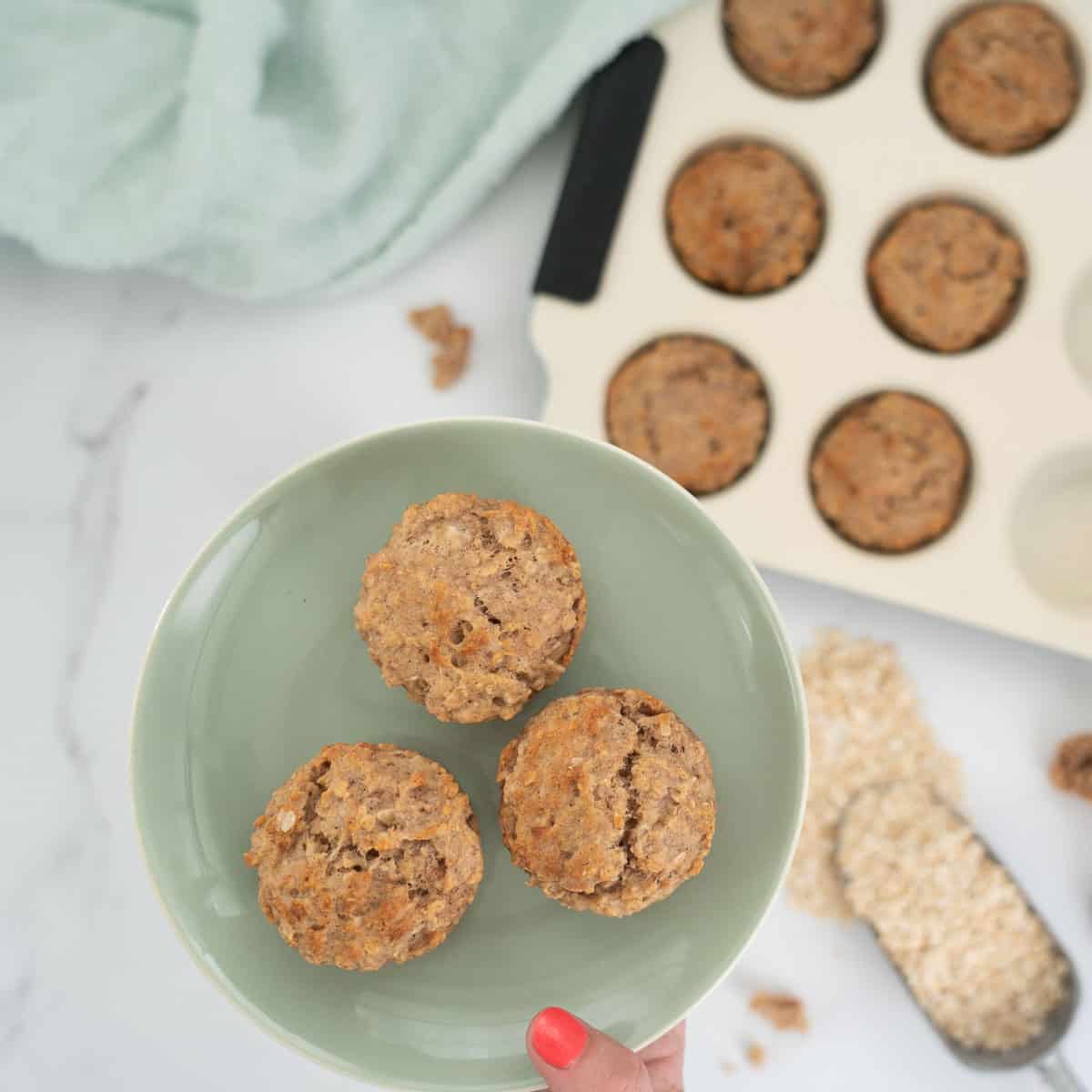 3 apple muffins on a pale green plate held above a kitchen bench.
