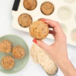Women's hand holding an apple toddler muffin above a kitchen counter top.