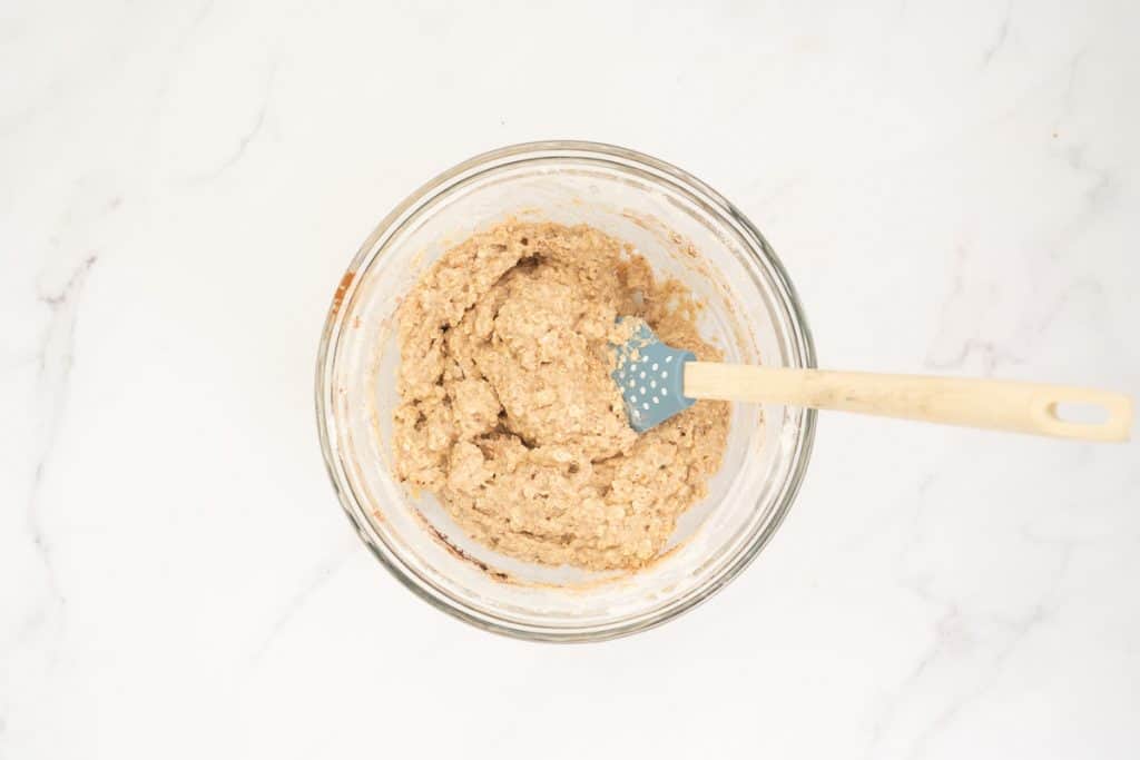 Muffin batter in a medium sized glass mixing bowl with a wooden handled spatula.