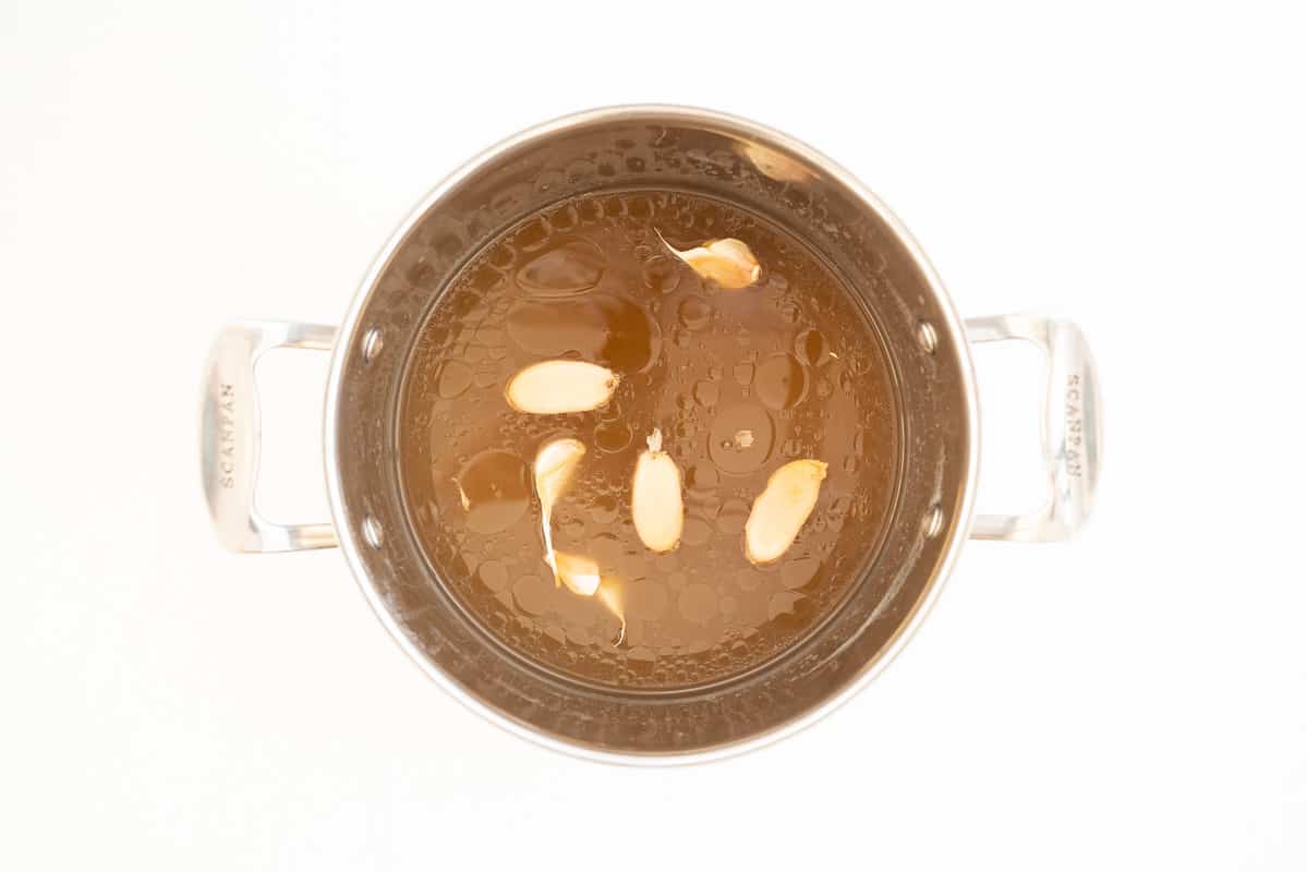 Broth in a large soup pot with garlic and ginger floating on top.