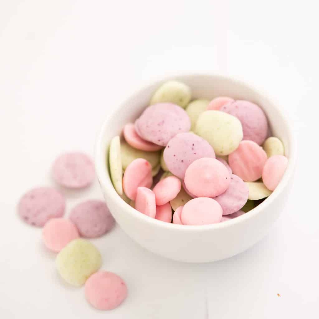 a small white bowl of baby yogurt melts in 3 colours, pale pink, lavender and pale green.