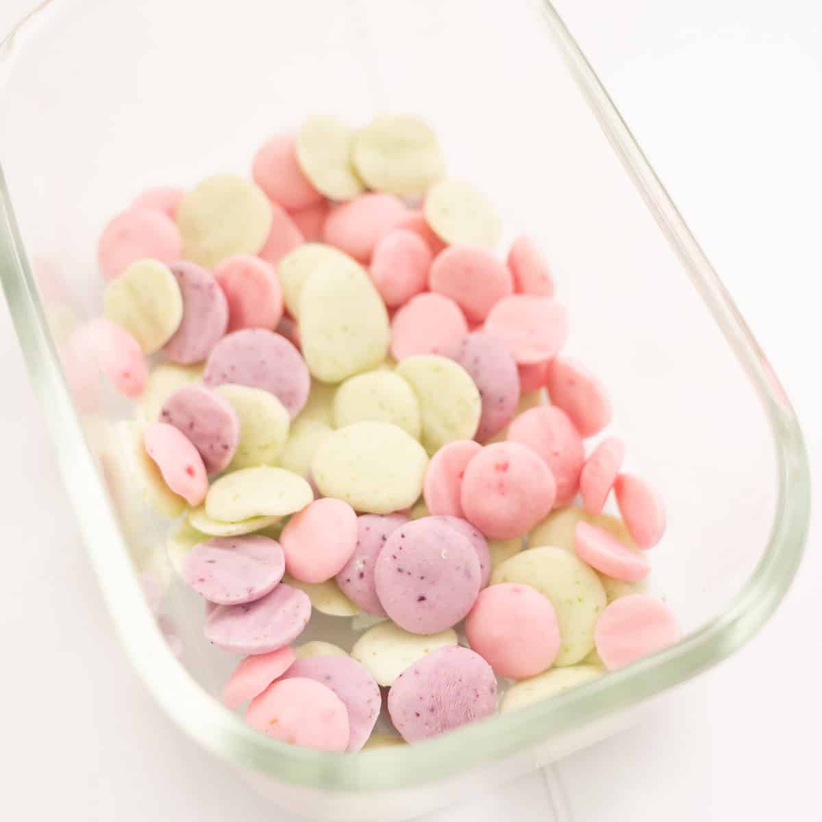 Three flavours (green, purple, pink) of baby yoghurt melts in a glass freezer container.