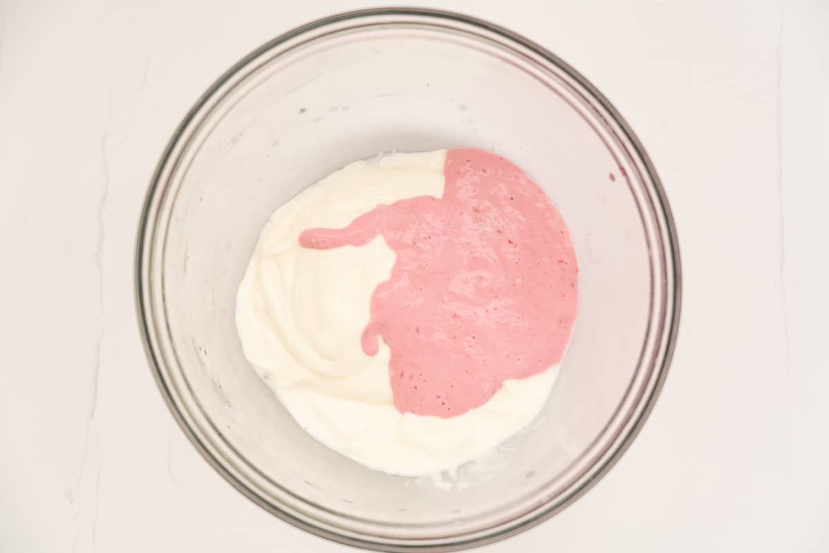 Pink raspberry purée in a mixing bowl with thick greek yoghurt.