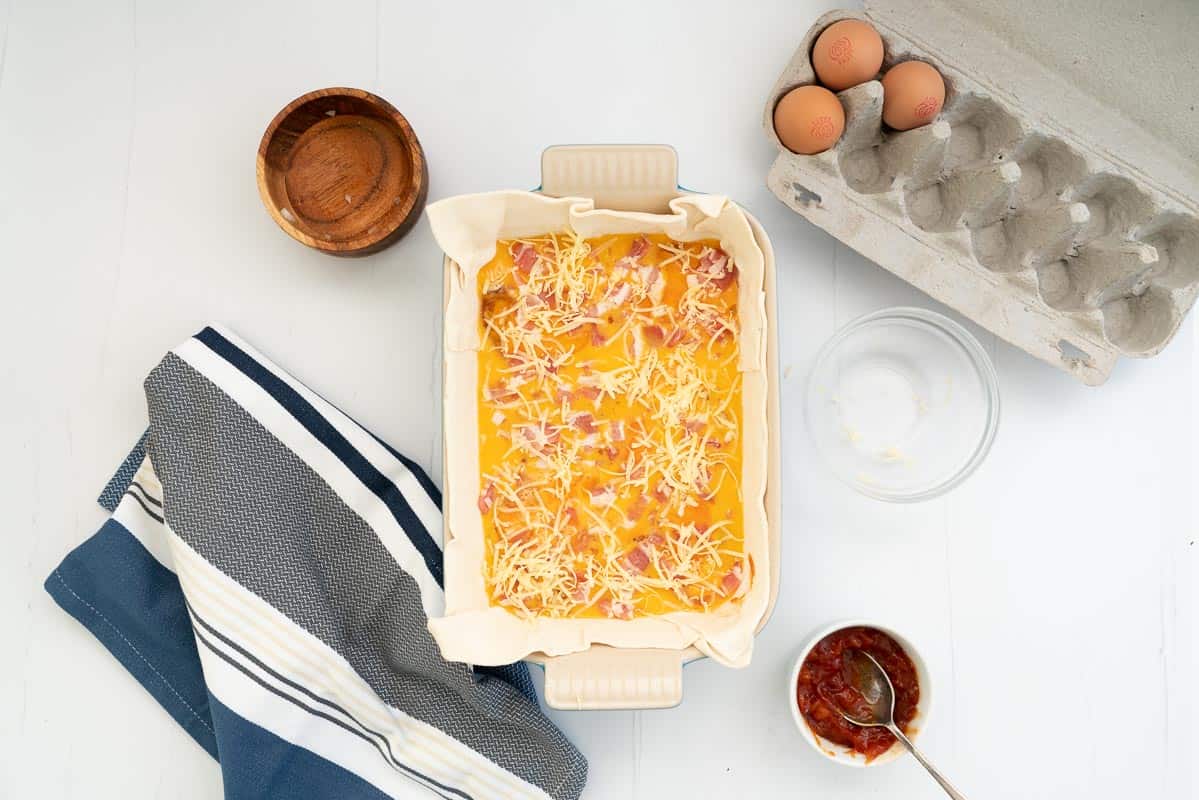 Grated cheese sprinkled on top of the fillings in a bacon and egg pie.