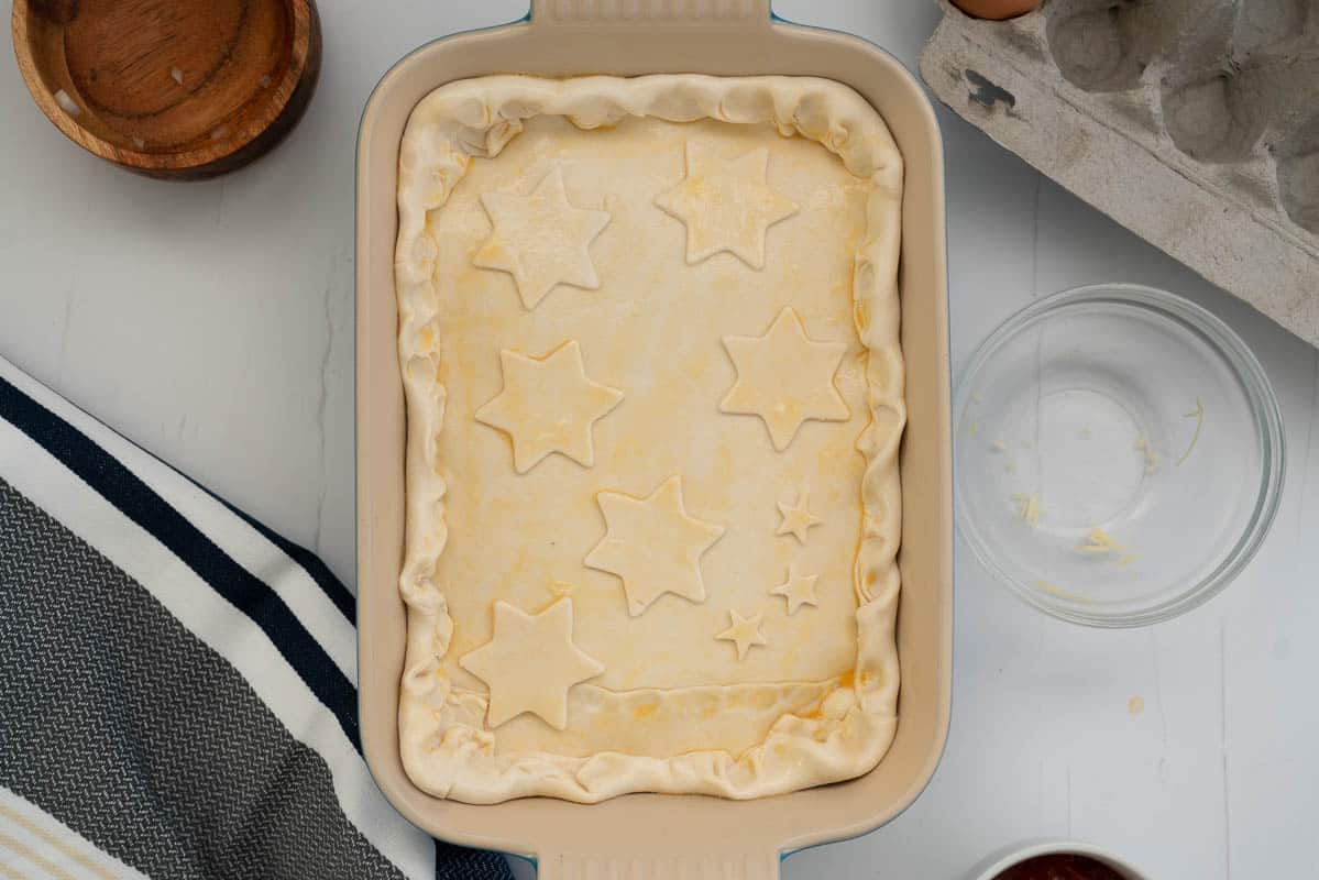 Uncooked pie crust decorated with stars and brushed with an egg wash.