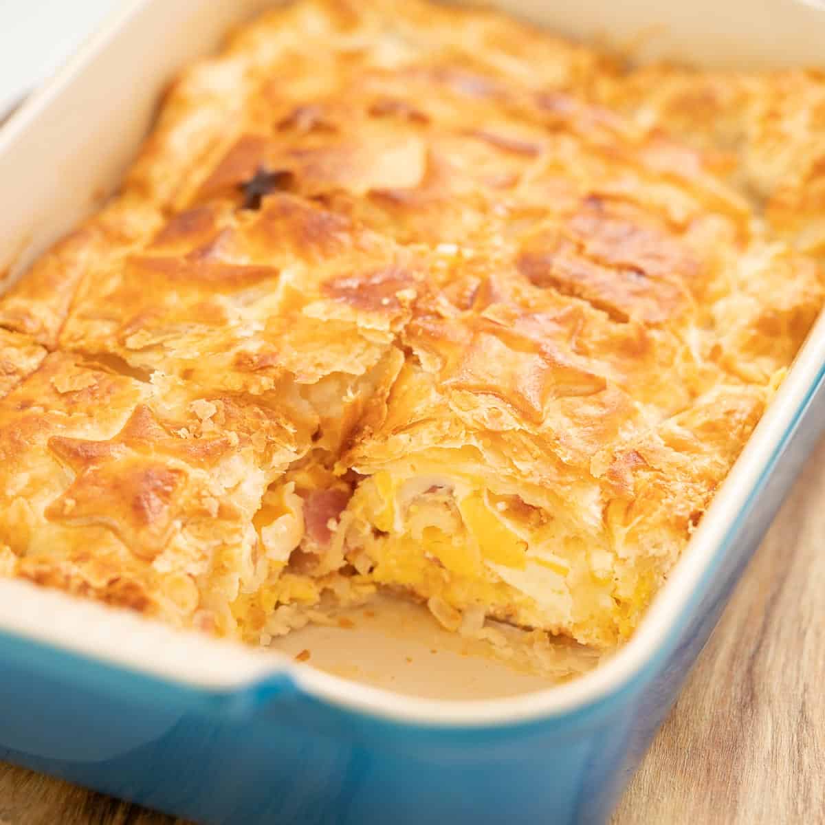Bacon egg pie in a blue rectangular pie dish, one square slice removed.