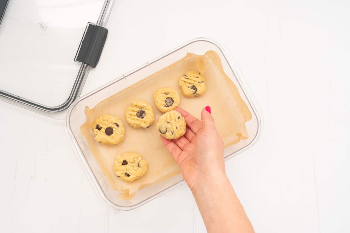 Cookie dough balls being placed in a baking paper lined container ready to freeze.