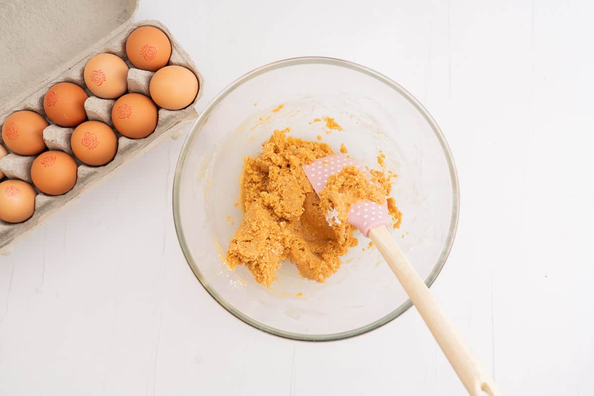peanut butter cookie dough in a glass bowl mixed with a pink spatula.