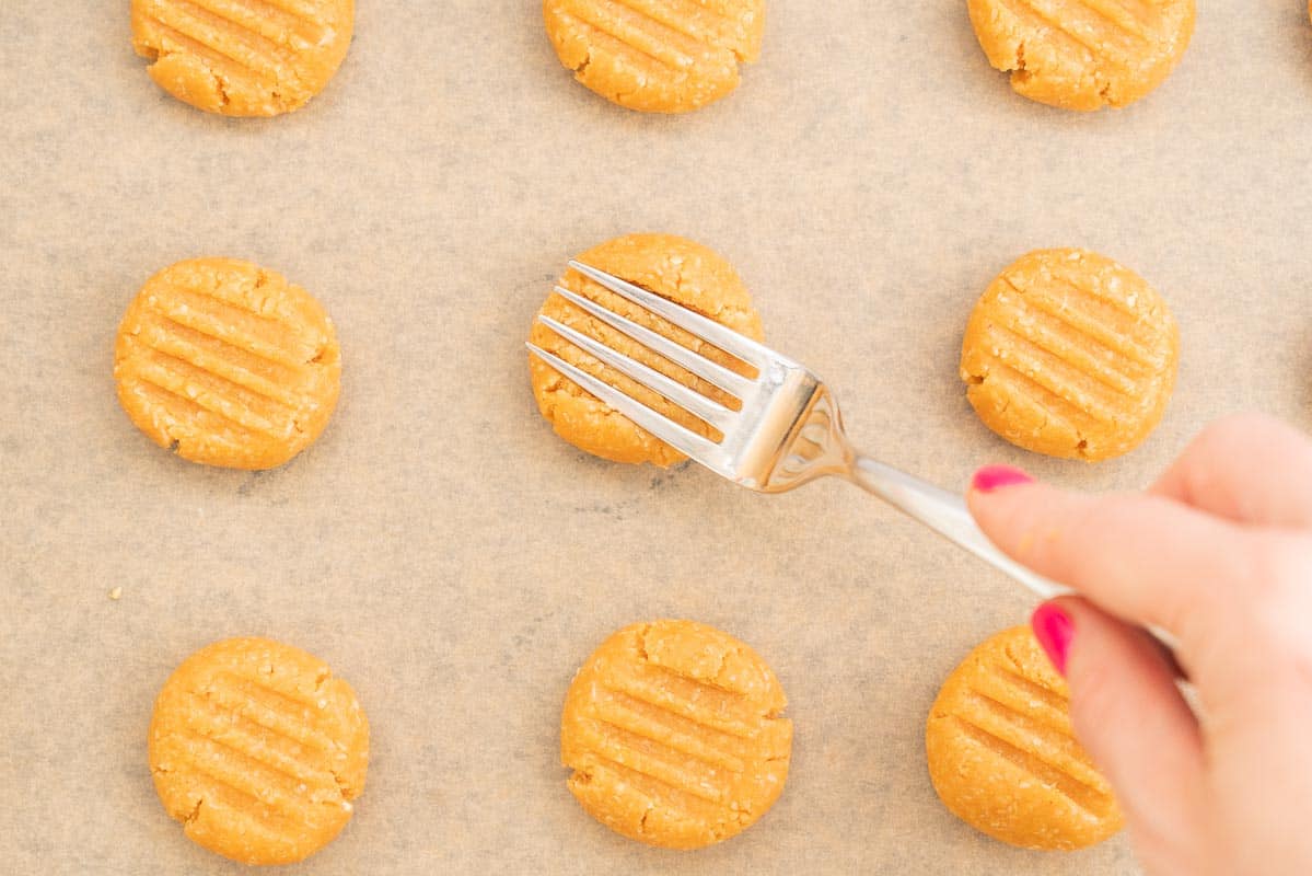 Women's hand pressing cookie dough balls with a fork.