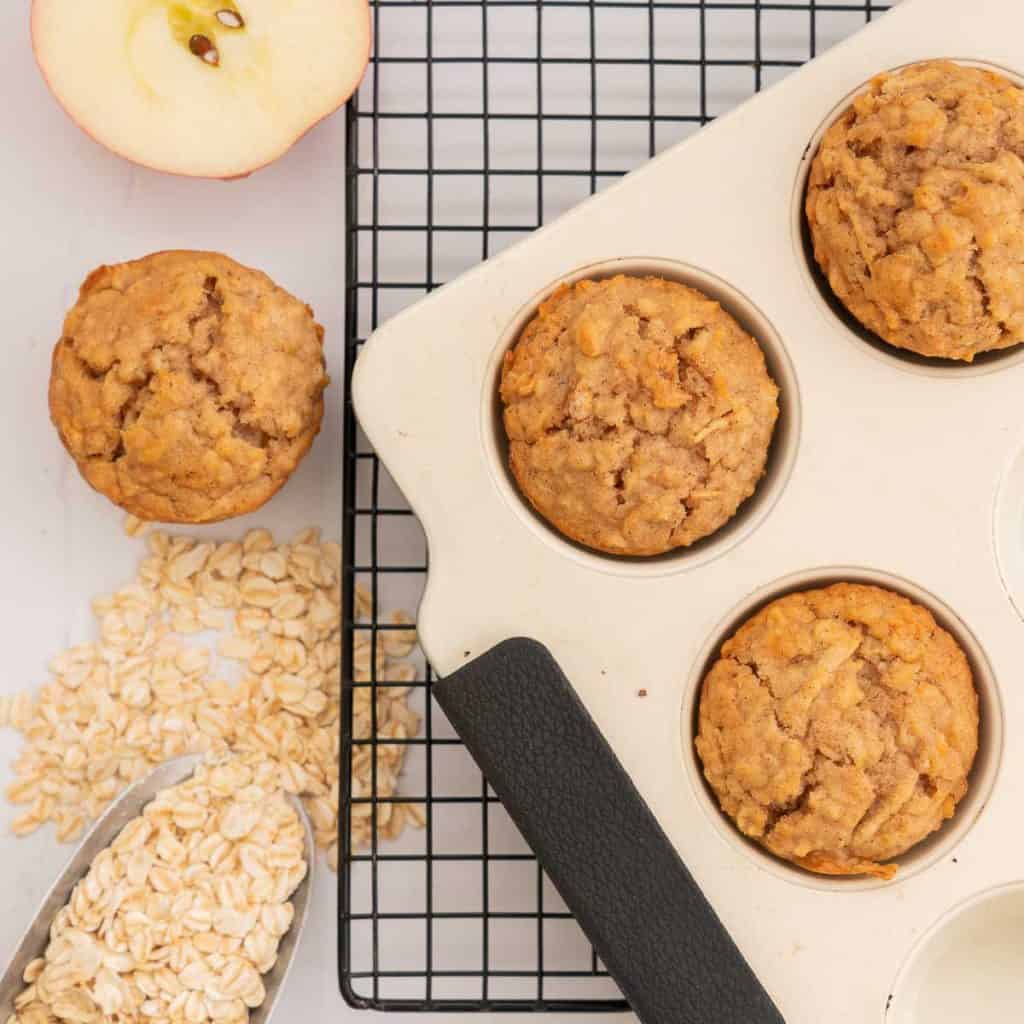 apple muffins in a cream muffin tray cooling on a black wire rack.
