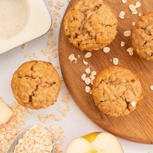 Over head shot of apple muffins on a wooden chopping board scattered with rolled oats.