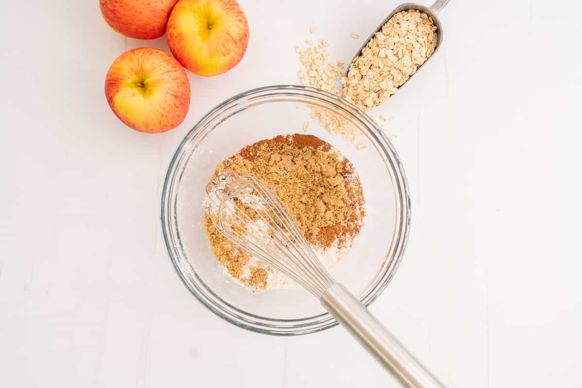Dry ingredients in a large glass mixing bowl being combined with a whisk.
