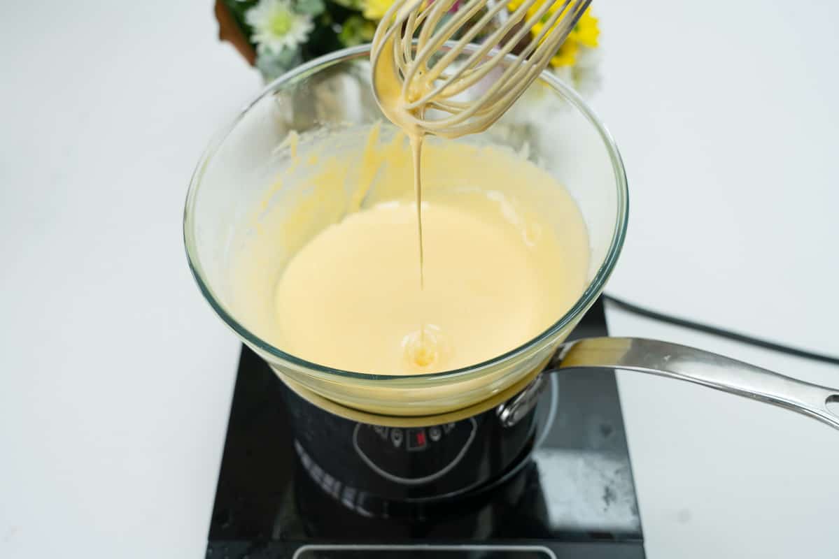Custard in a glass bowl on top of a double boiler. Pale, and thickened,