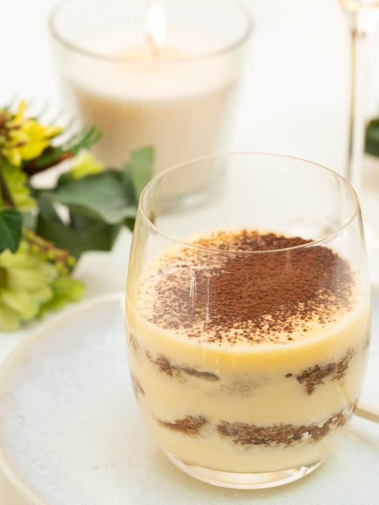 Tiramisu served in a glass, a candle, and flowers in the background.