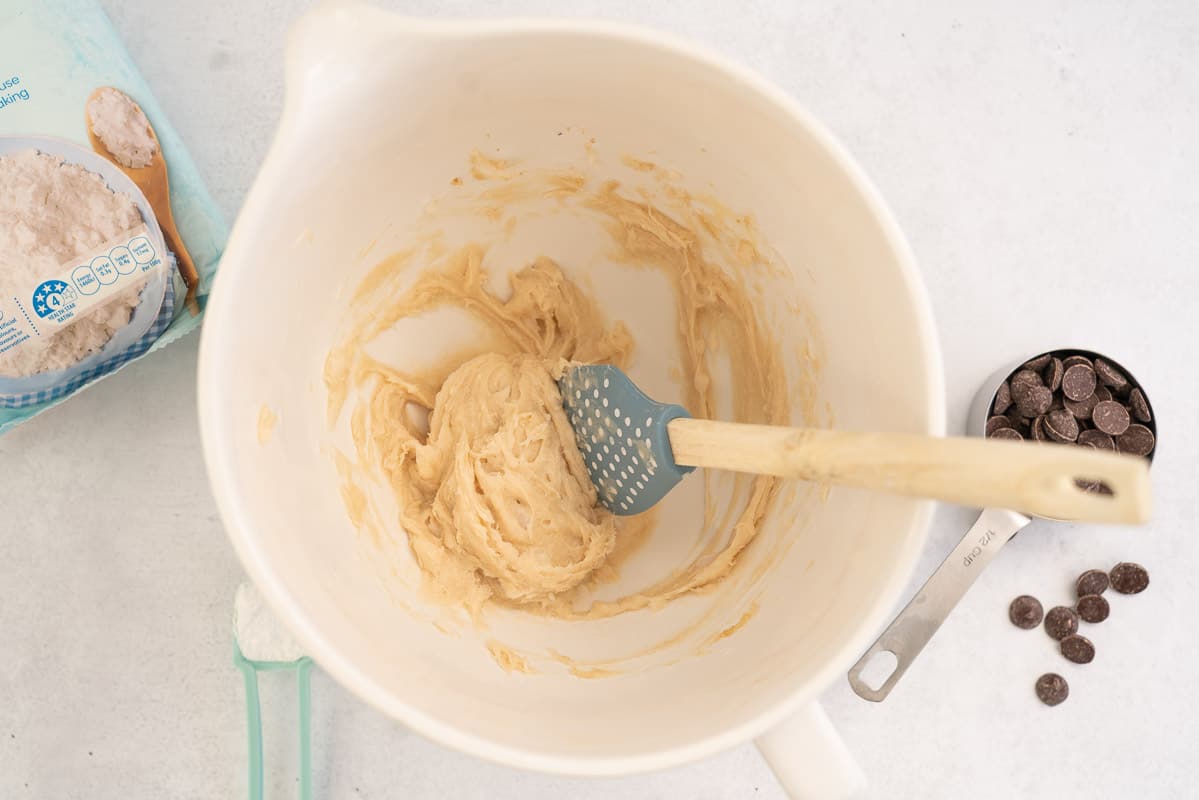 Creamed coconut oil and sugar in a white ceramic mixing jug with a blue spatula.