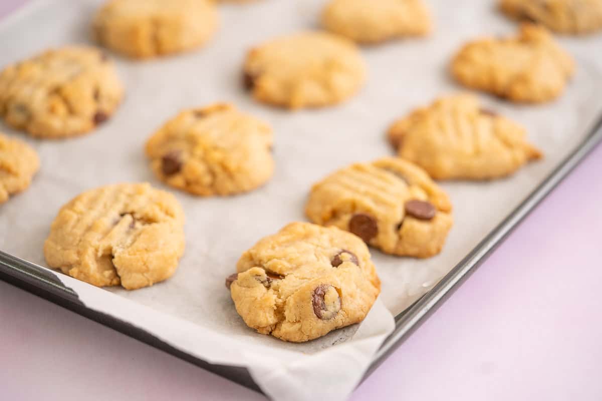 Golden baked chocolate chip cookies on a baking paper lined cookie sheet.