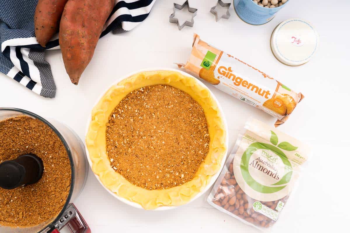 Pastry case in a pie dish with a layer of gingernut biscuit crumb pressed in the base.