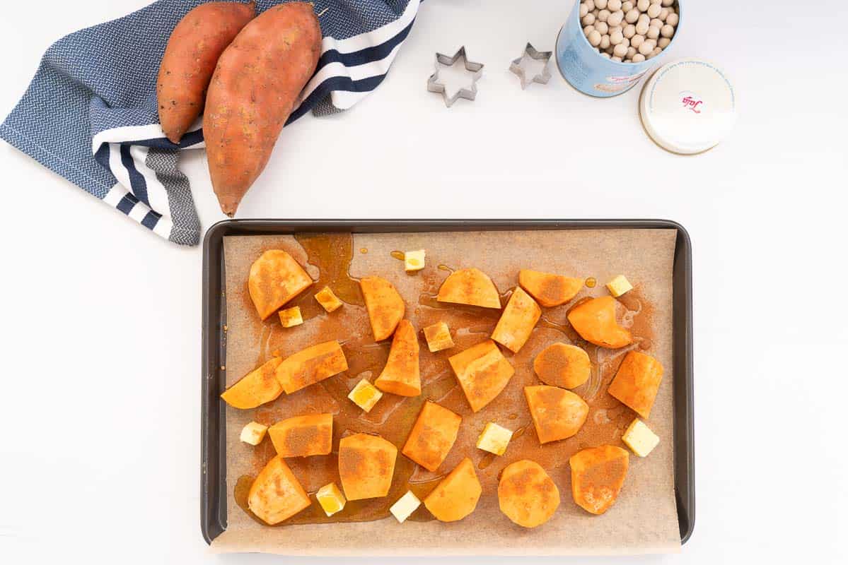 Pieces of sweet potato on a lined tray dusted with spices, and drizzled with maple syrup.