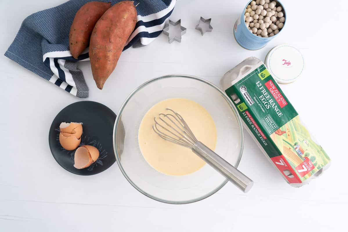 A large glass mixing bowl of egg and cream with a whisk.