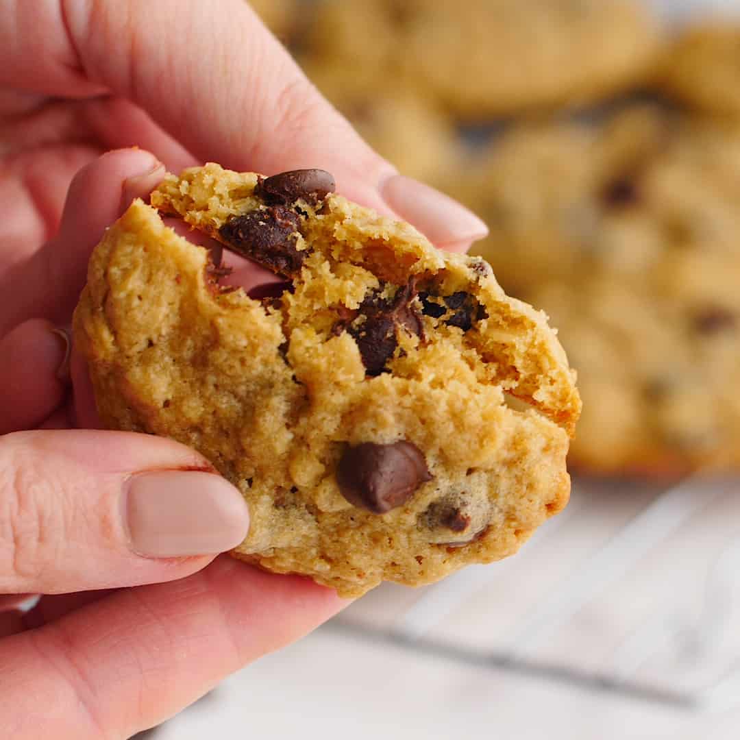 A woman's hand breaking a cookie in half to reveal oatmeal and chocolate drops.