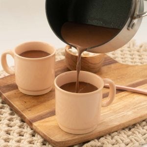 Hot chocolate being poured from a saucepan into a pink mug.