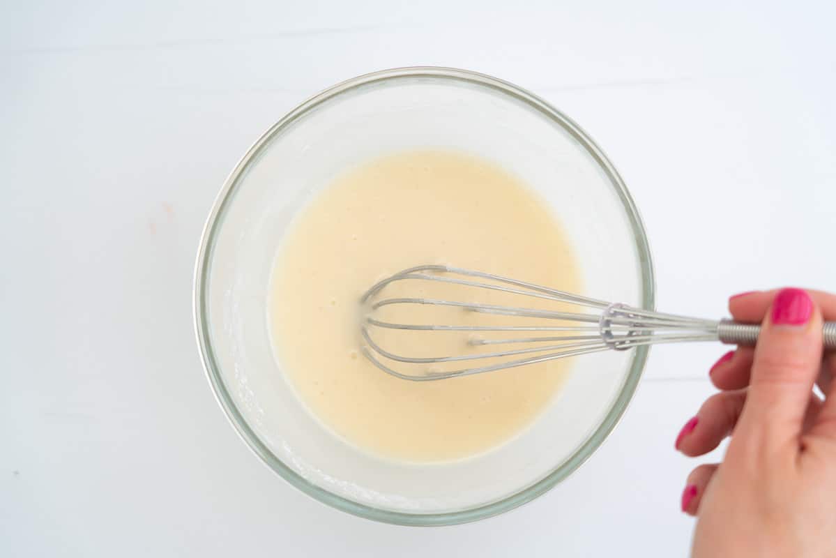 A small bowl of white glaze being whisked by a woman's hand.