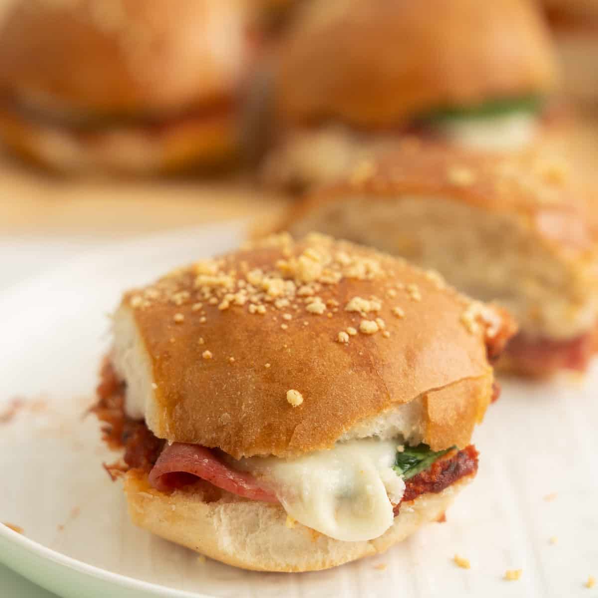 A pizza slider sitting on a white plate, melted mozzarella oozing from the bun.