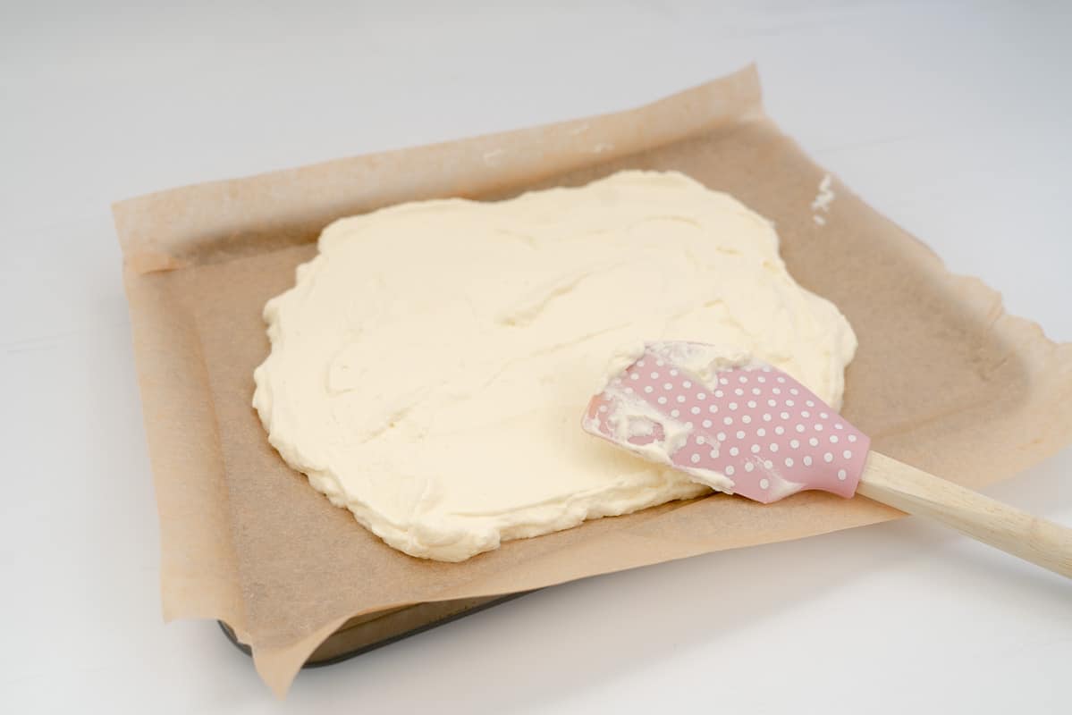 Whipped cream spread out on a baking paper lined tray.
