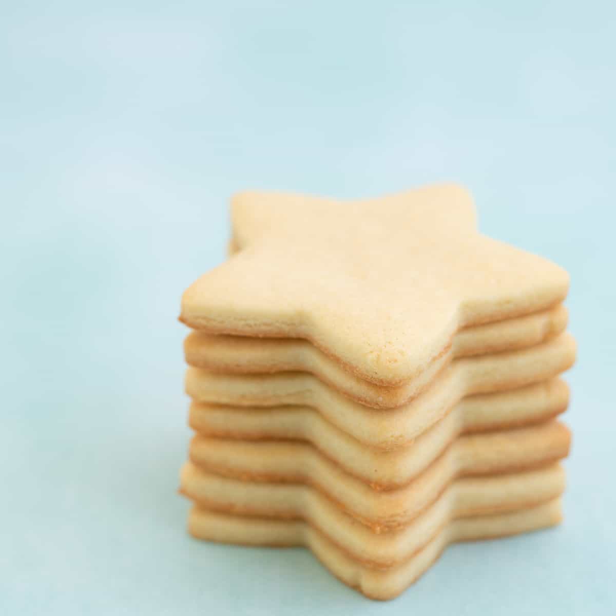 Seven star shaped sugar cookies stacked in a tower on a mint green background.