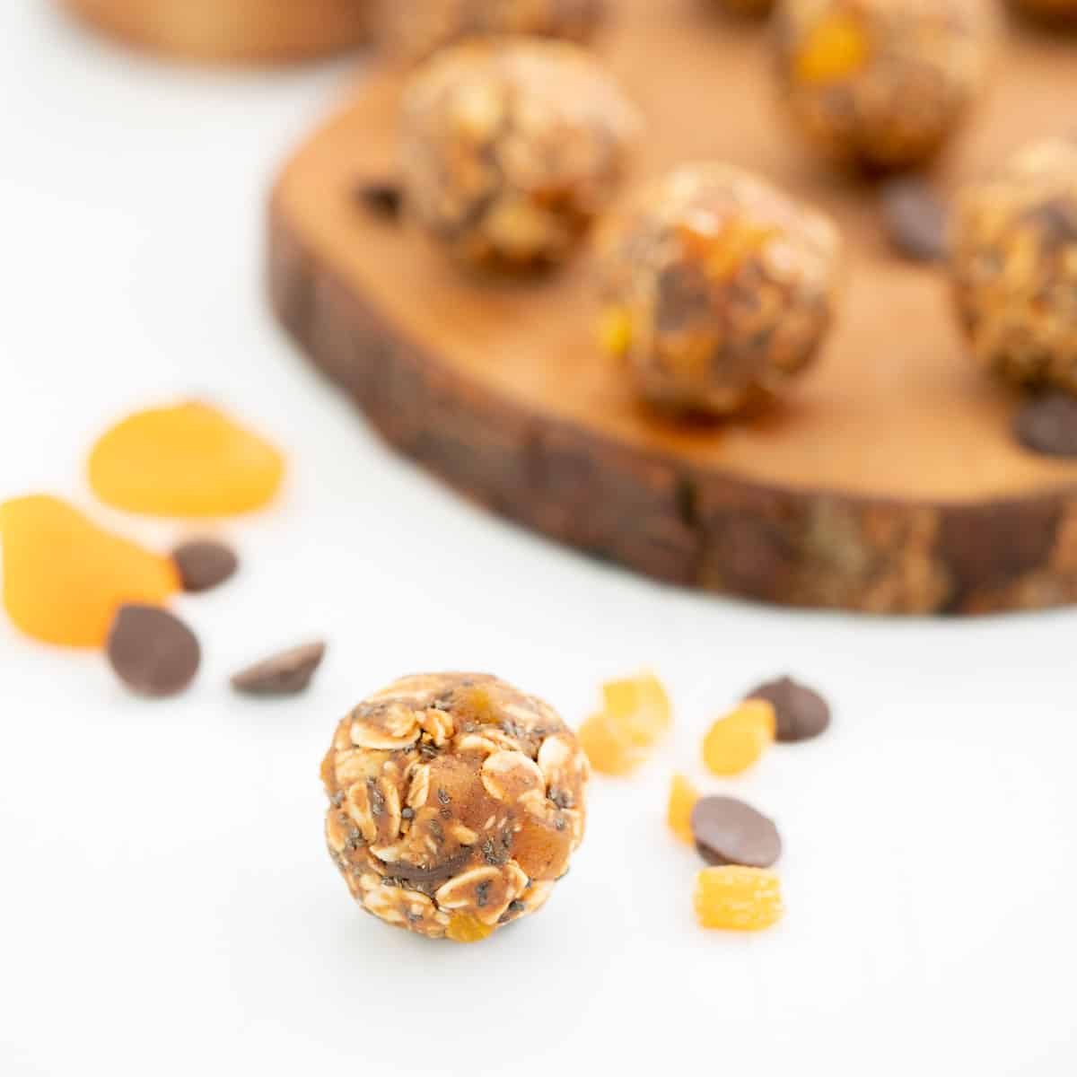 An apricot ball on a white bench top with a wooden tray of more apricot balls in the background.