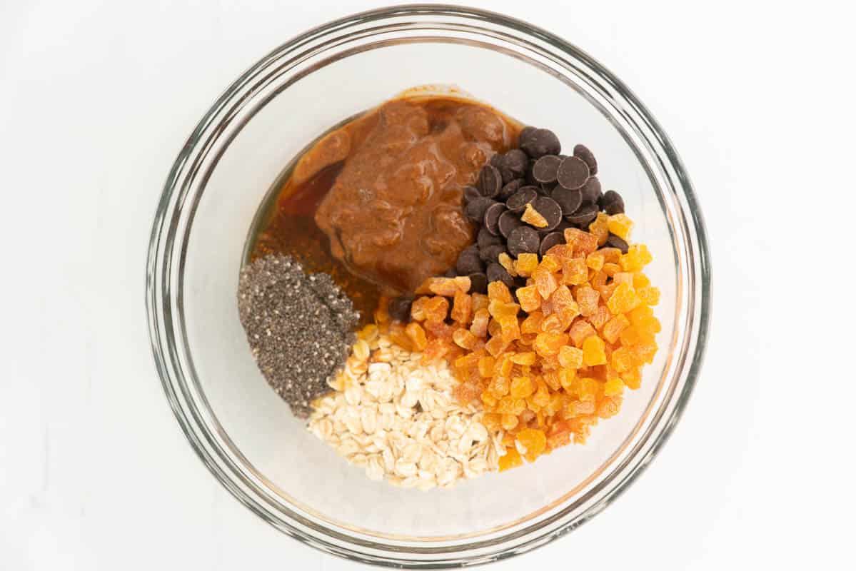Oats, dried apricots, chia seeds, chcocoalte chips and nut butter in a mixing bowl.