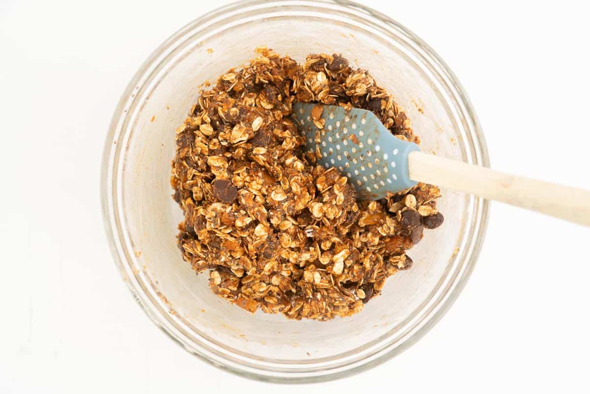 Apricot ball mix resting in a glass mixing bowl with a blue spatula.