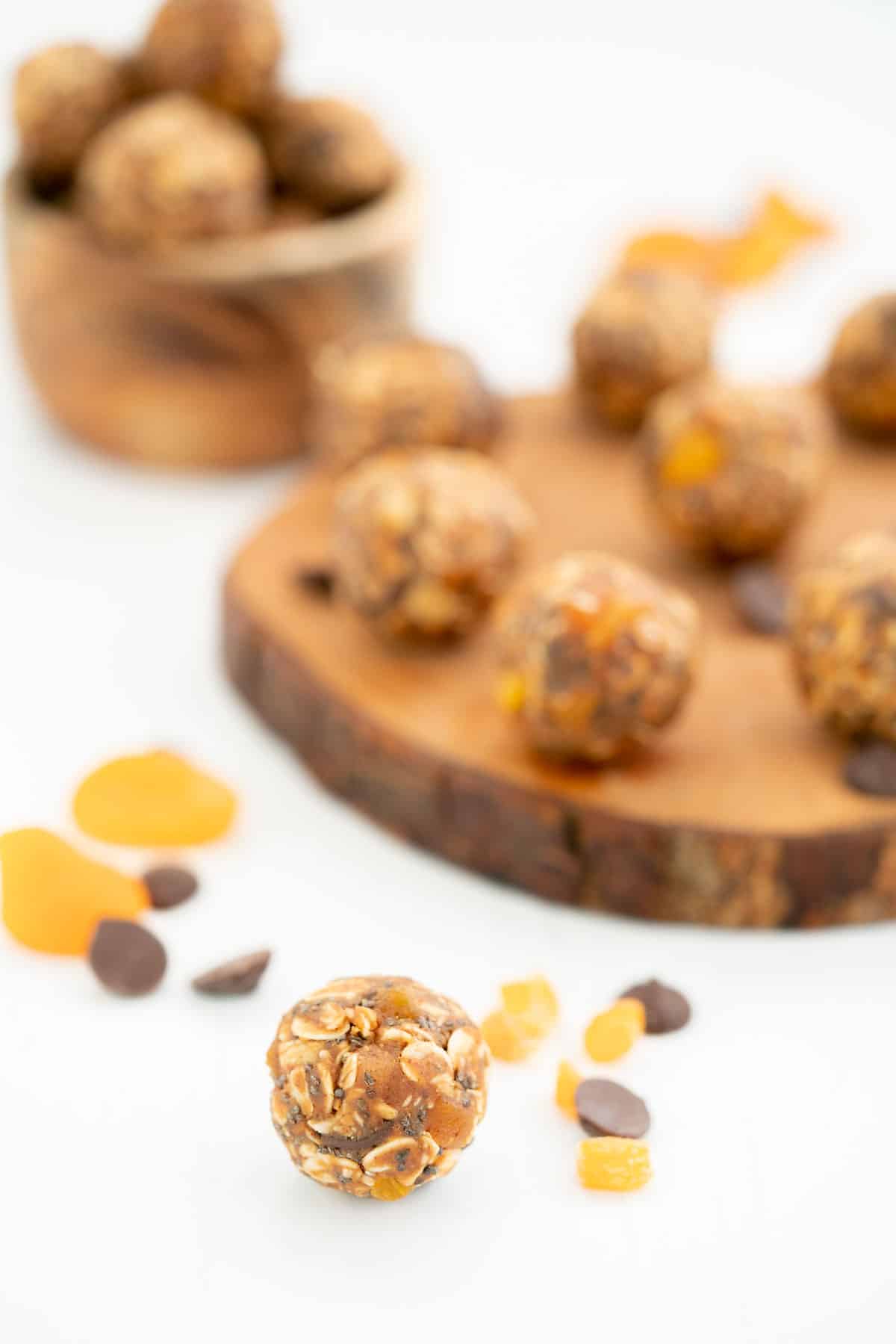 An apricot ball on a white bench top with a wooden tray of more apricot balls in the background.