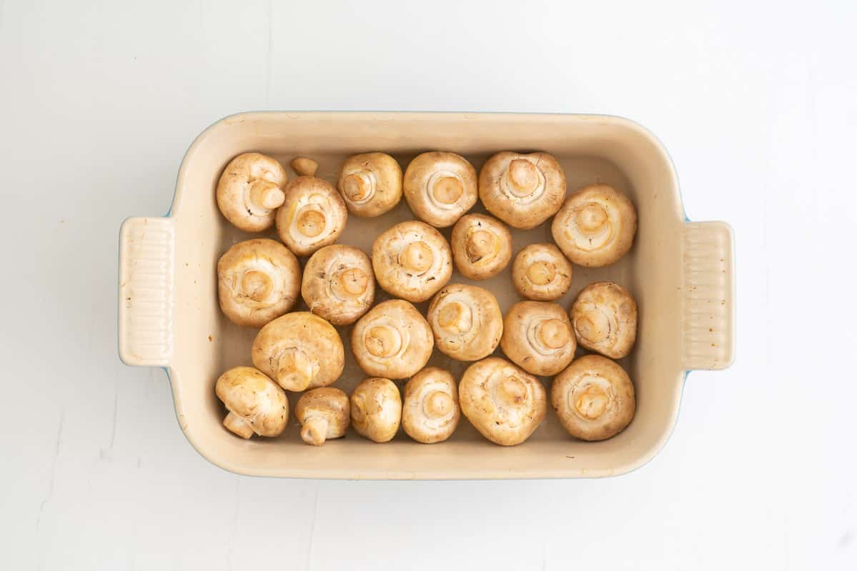 A rectangular baking dish filled with olive oil coated button mushrooms.