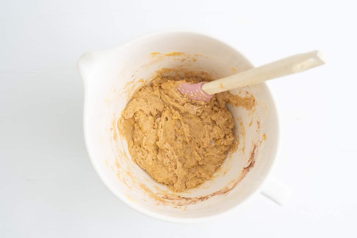 Banana cake batter in a large white mixing jug with a pink spatula.