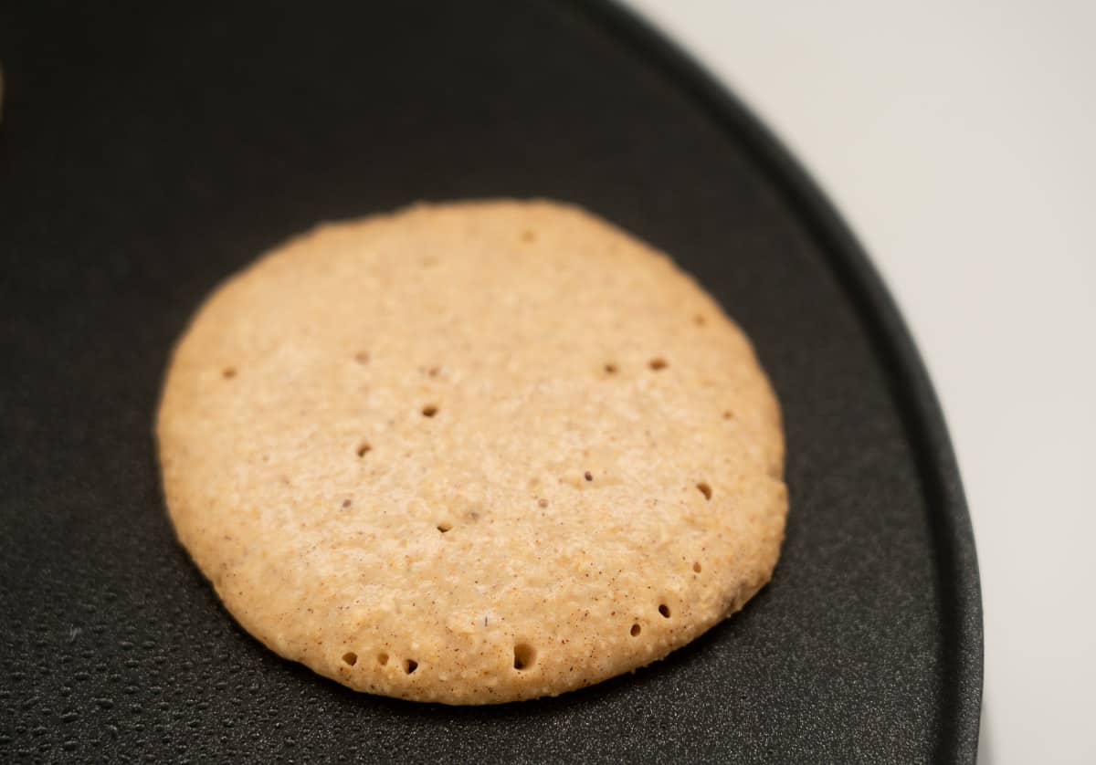A small pancake on a hot plate, bubbles visibly forming on the top of the pancake