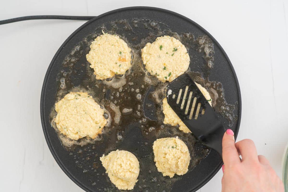 Cauliflower fritter mix being flattened into a patty shape with a spatula.