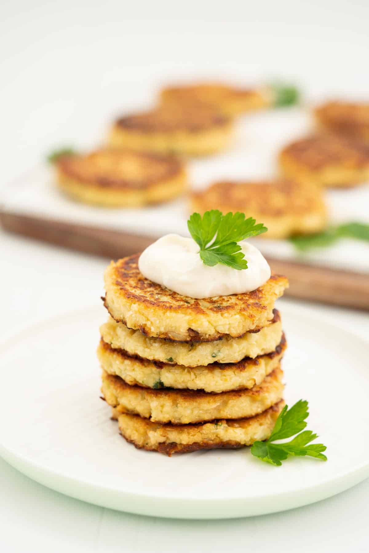 A stack of 5 cauliflower fritters topped with aioli and parsley.