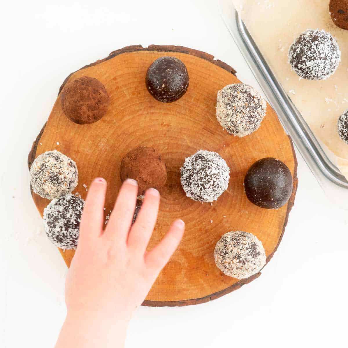 A child's hand reaching for a chocolate bliss ball.