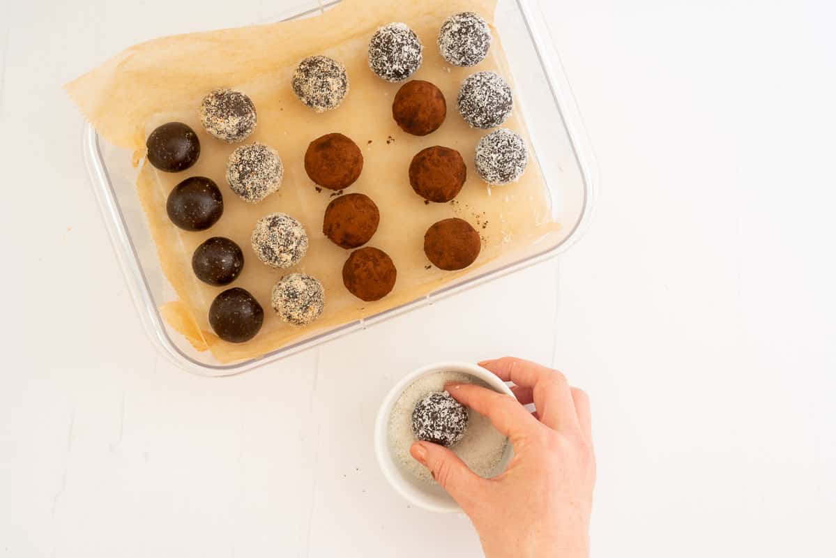 A woman's hand rolling a chocolate date ball in a bowl of desiccated coconut.