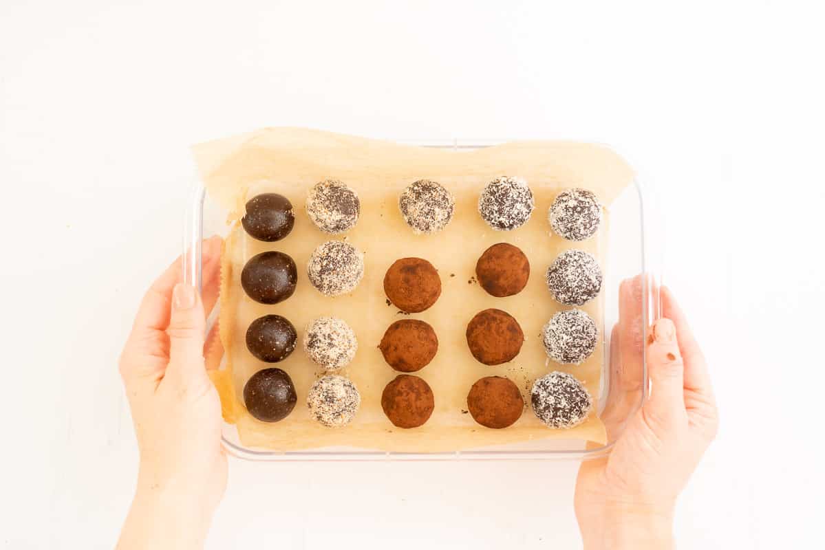A selection of chocolate bliss balls rolled in coconut, cocoa and ground almonds in a container ready to be refrigerated.