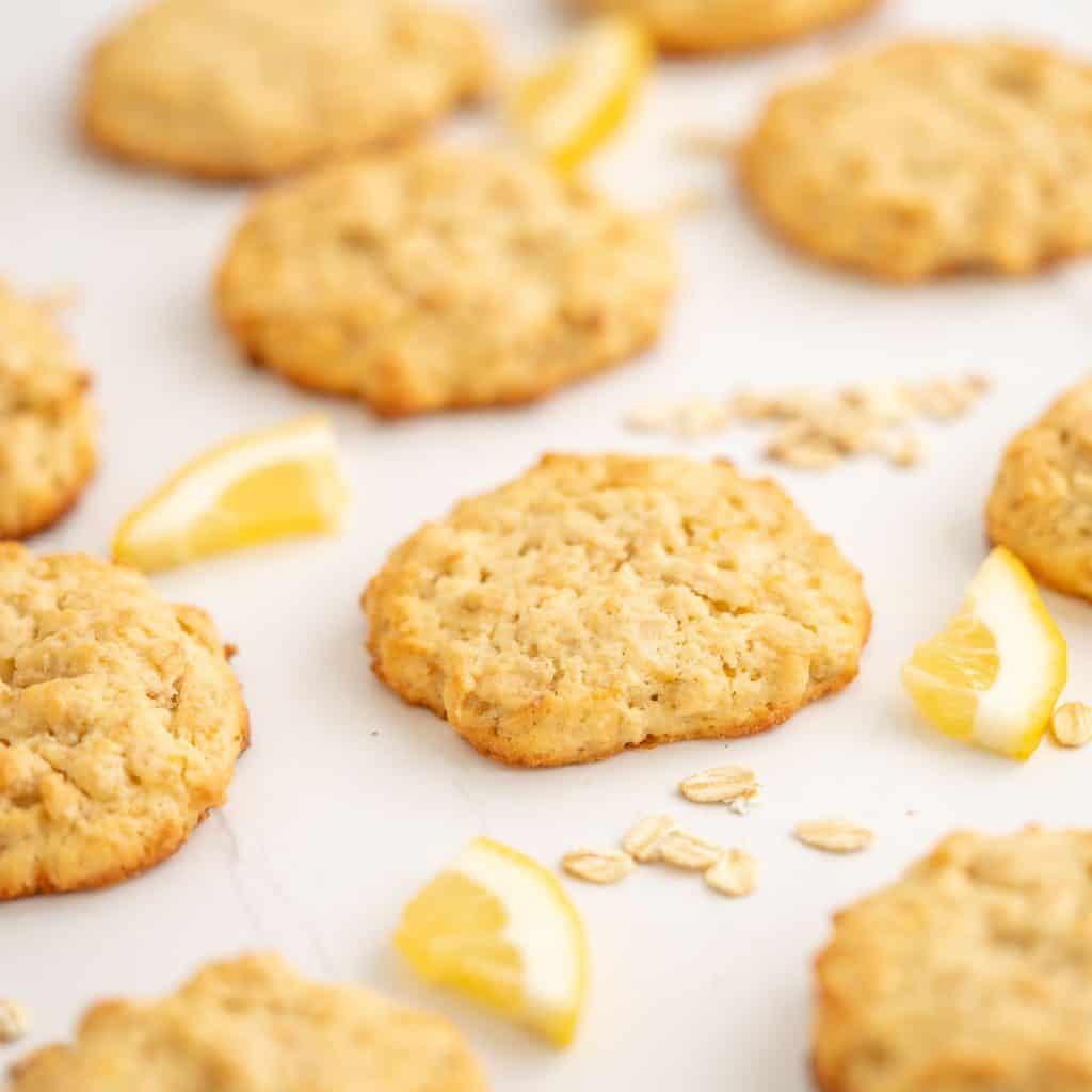 A lemon oat cookie on a white bench top with scattered rolled oats and lemon pieces.