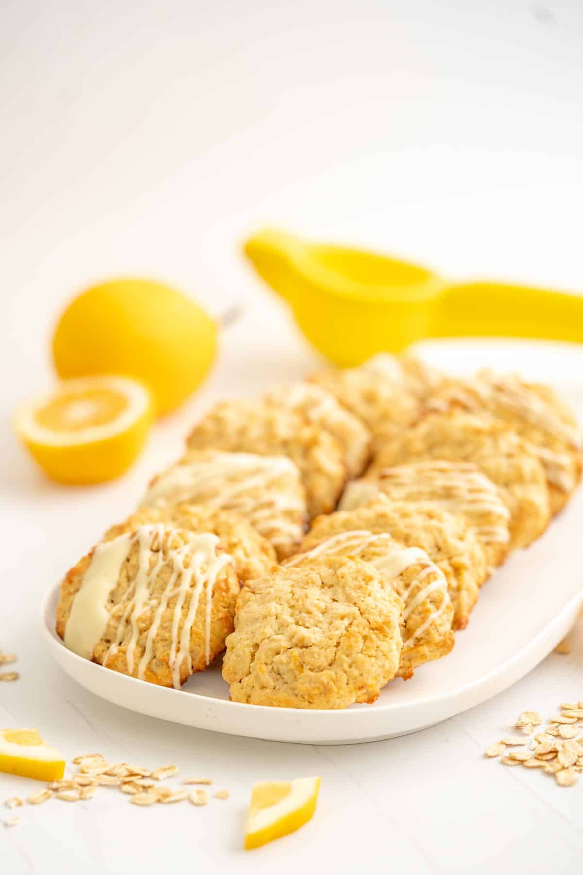 A white platter with 16 oatmeal lemon cookies, lemons and a lemon squeezer in the background.