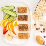 4 Peanut butter bars and chopped fruit and veggies on a white platter.
