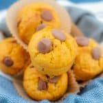 Pumpkin chocolate chip muffins in a bowl lined with blue cloth.