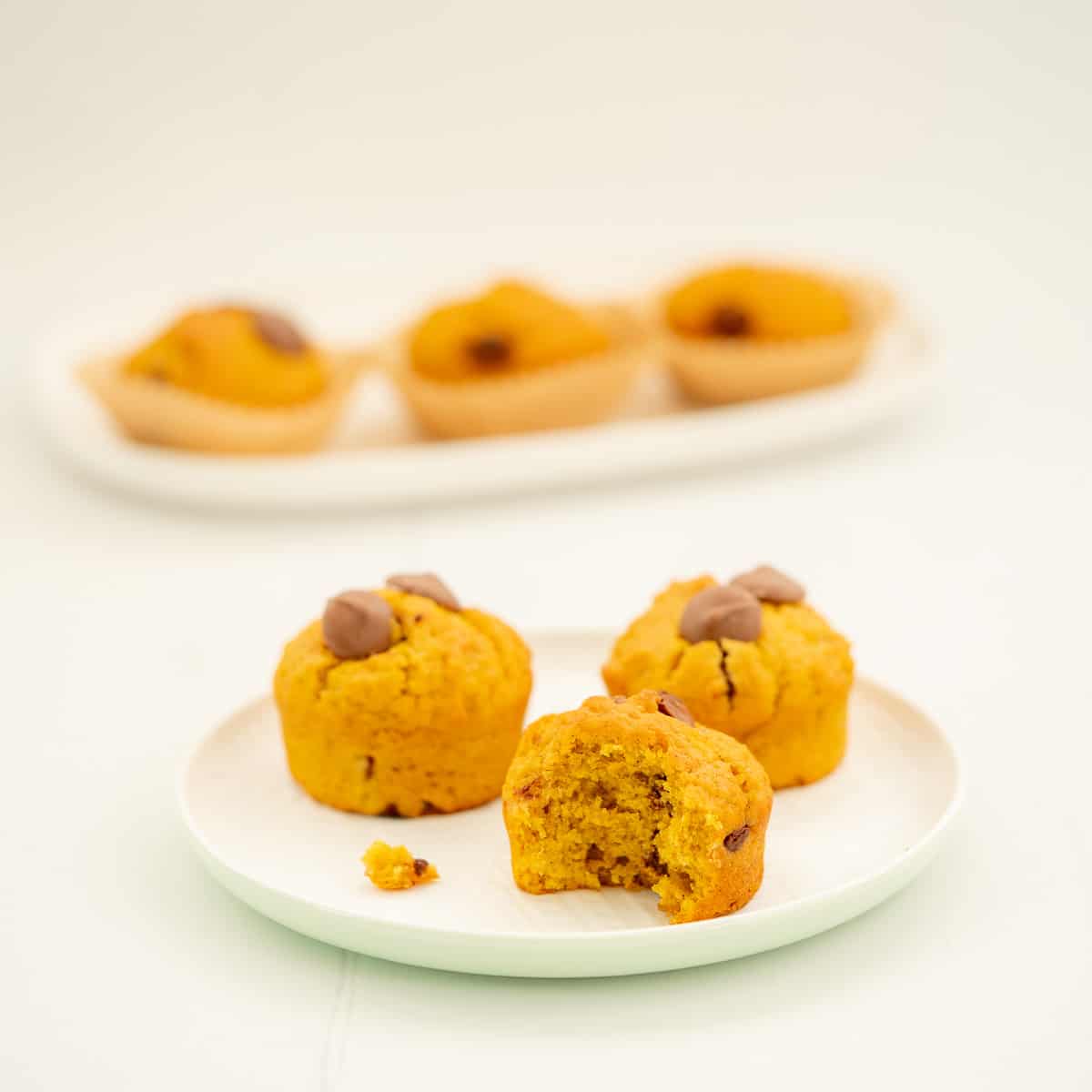 3 pumpkin chocolate chip muffins sitting on a white ceramic plate.