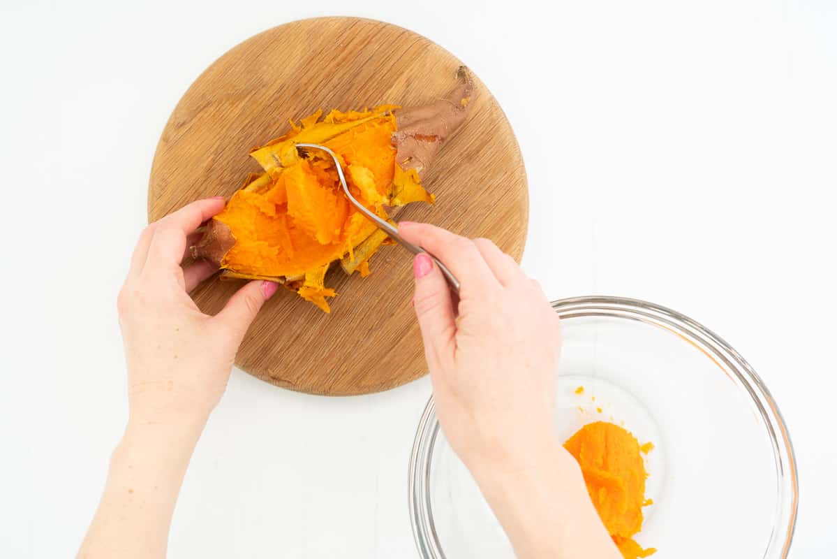 Hands removing the soft cooked flesh of a sweet potato