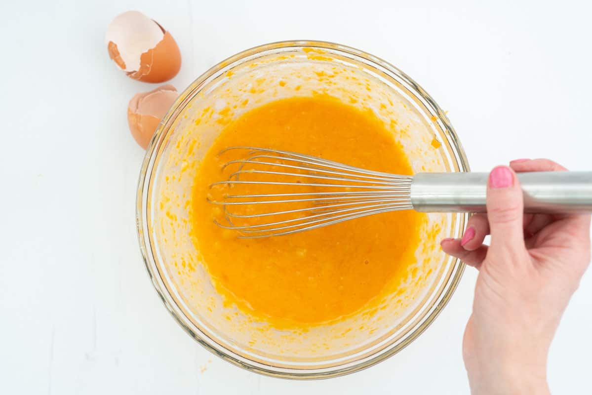 A glass mixing bowl filled with wet ingredients being whisked together.